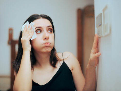 homeowner wiping forehead looking at thermostat